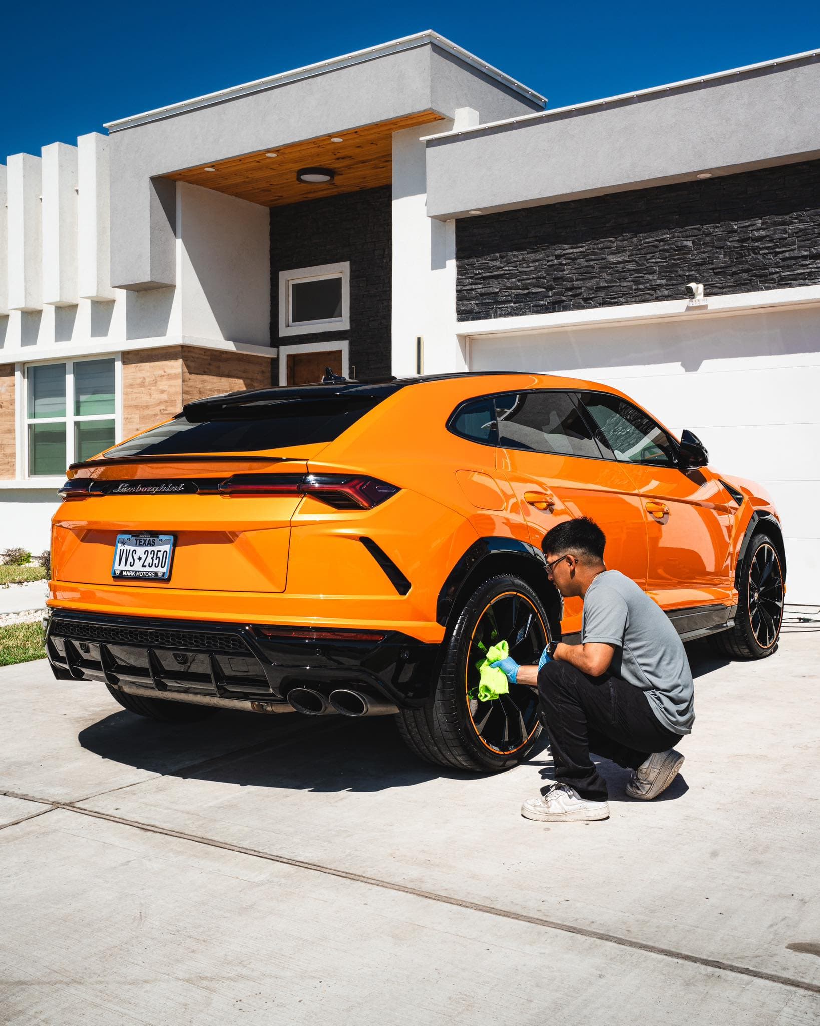 Detailer hand-finishing the wheels of an orange Lamborghini Urus in a driveway